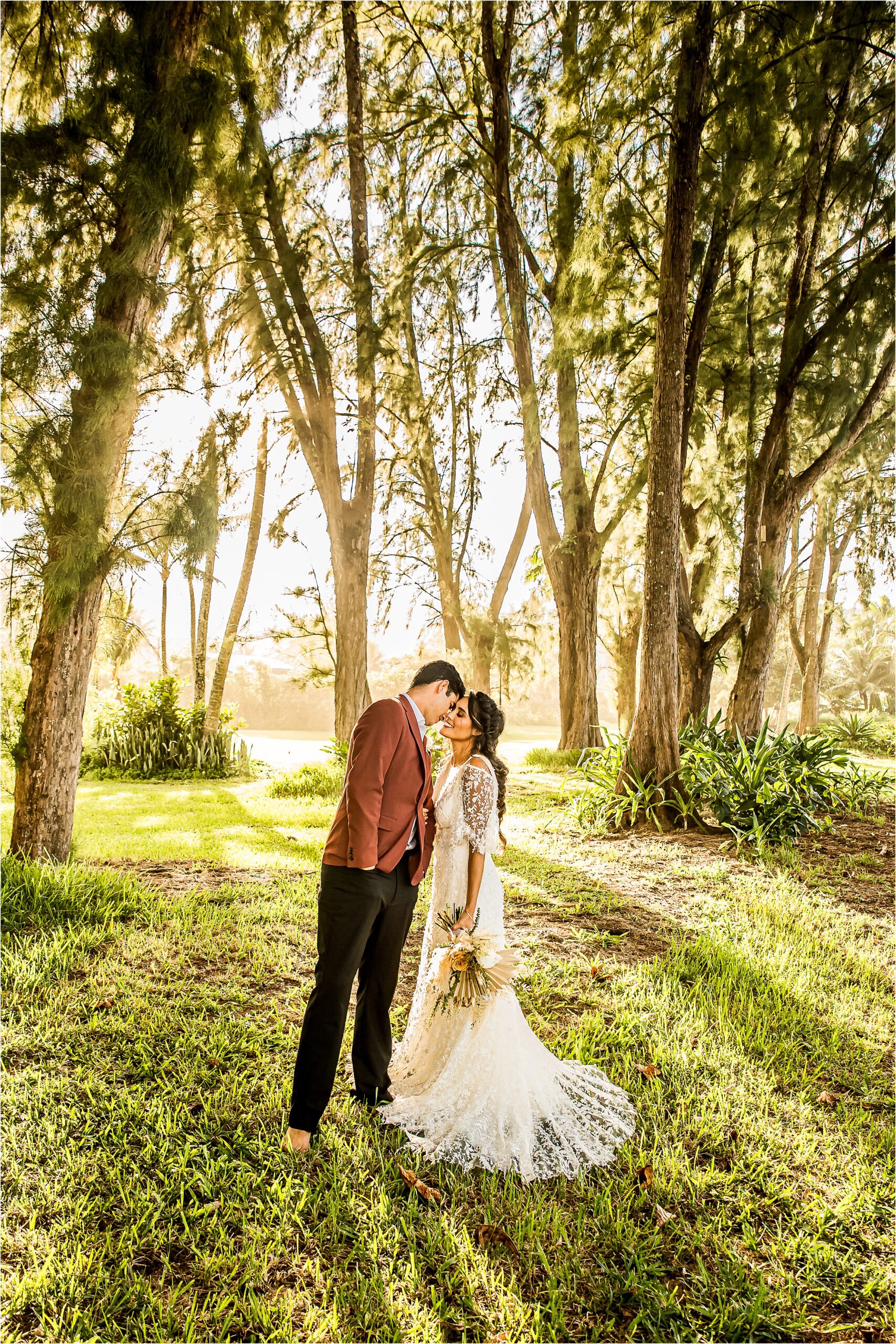 man and woman forehead to forehead in wedding attire with trees in the background
