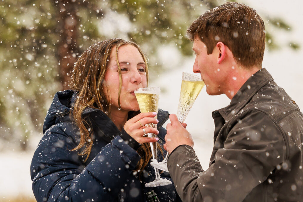 engagement cheers with chamapgne following surprise proposal in the snow in Colorado