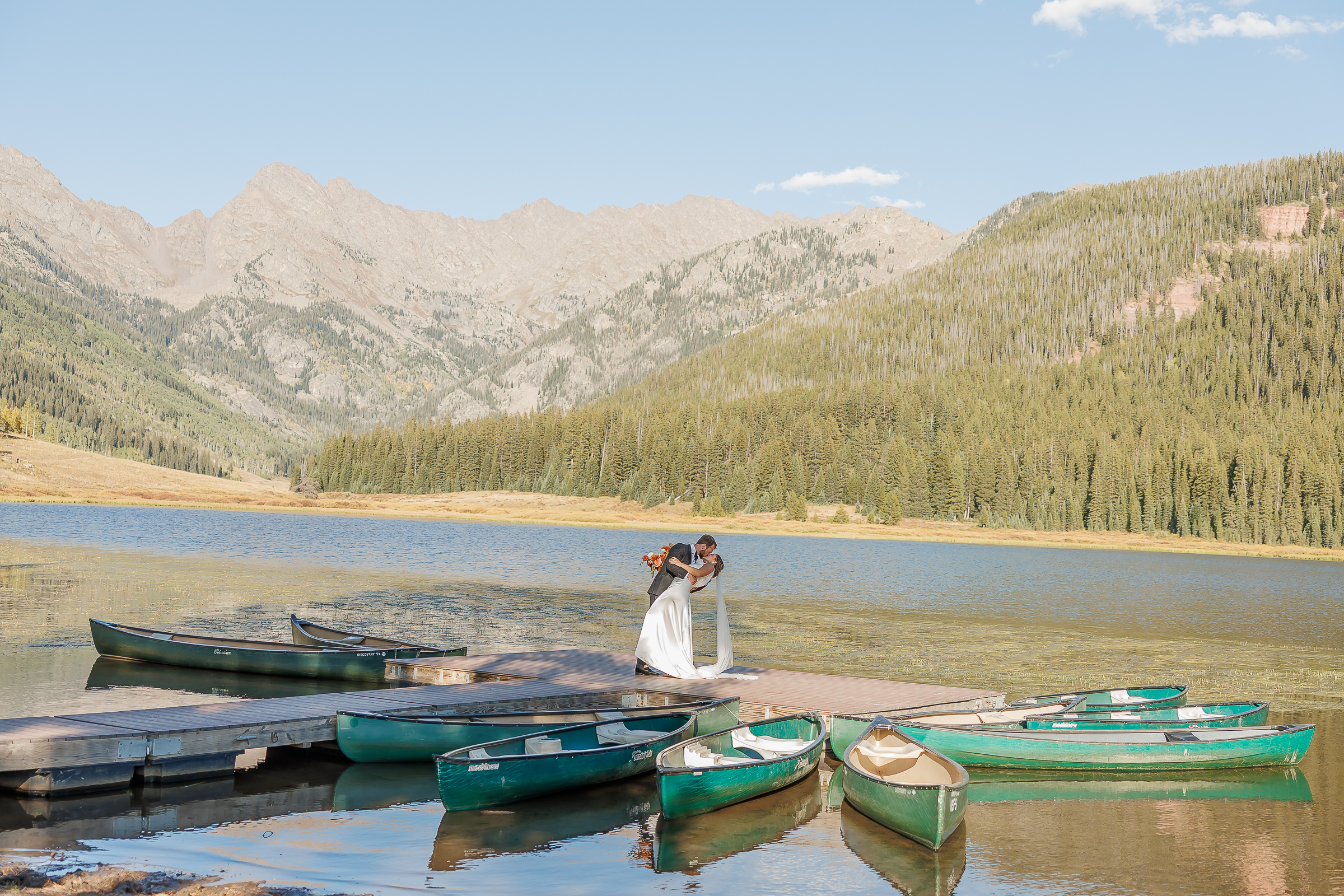 groom dips bride for a kiss as wedding photographer captures them and the sprawling vail mountain view in the background